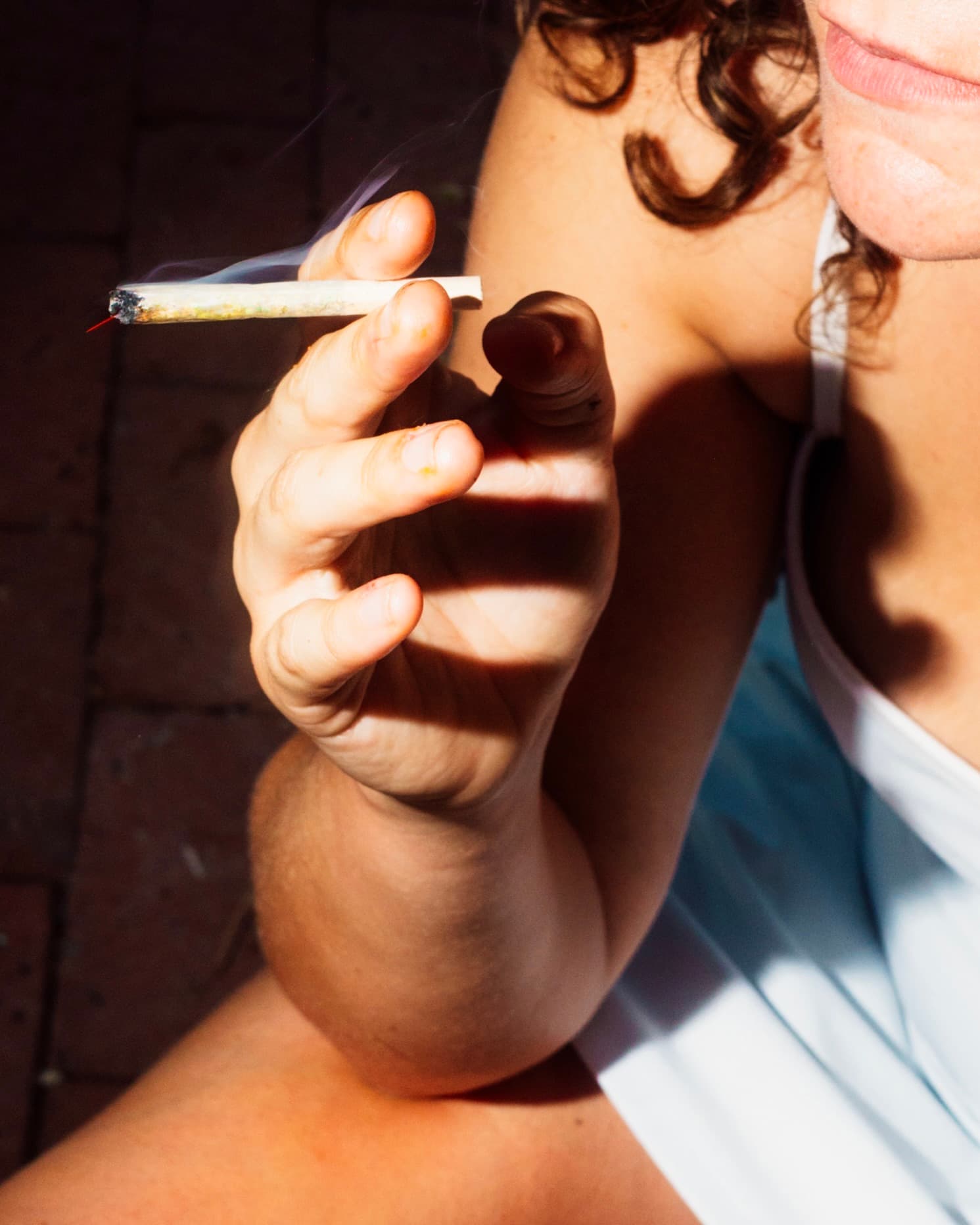 A hand holding a lit joint in afternoon sun over brick
